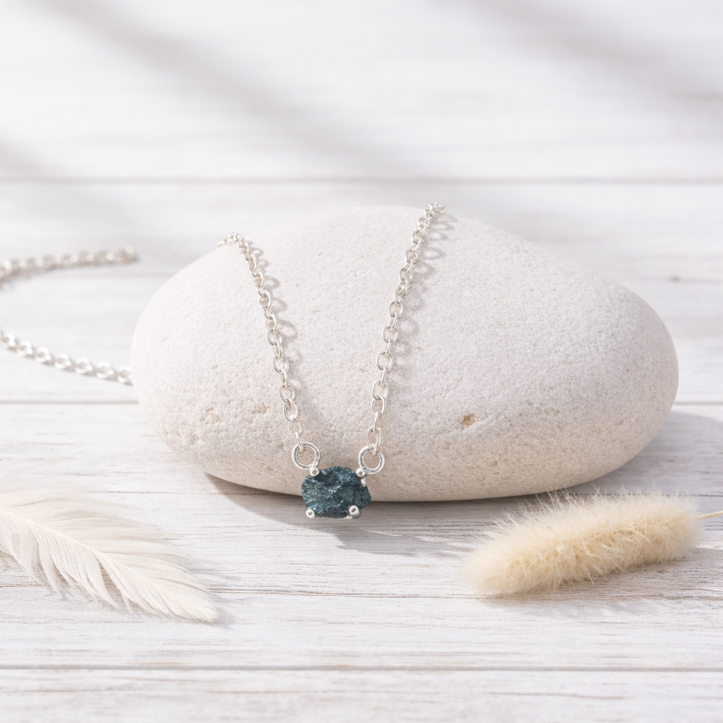 Silver necklace with a raw blue diamond on a white stone surface