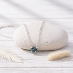 Silver necklace with a raw blue diamond on a white stone surface
