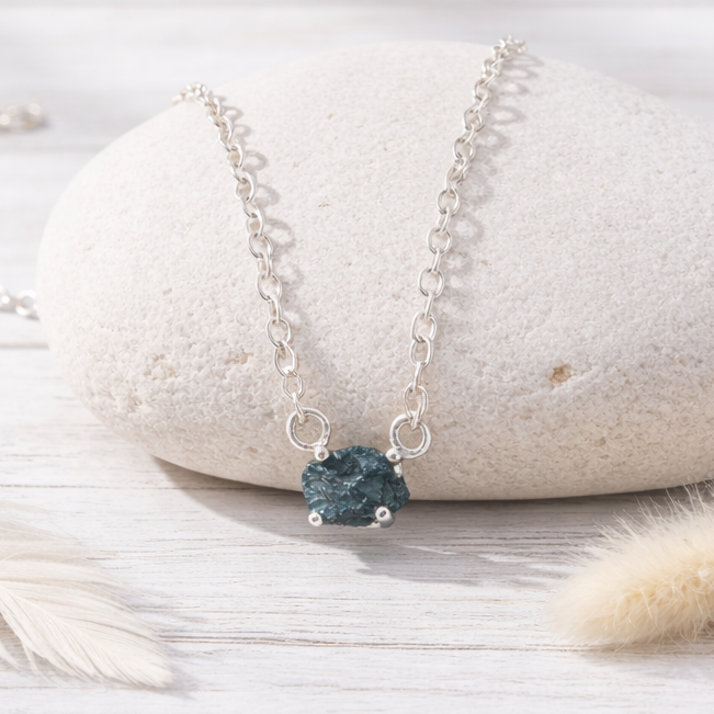 Silver necklace with a raw blue diamond on a white stone surface