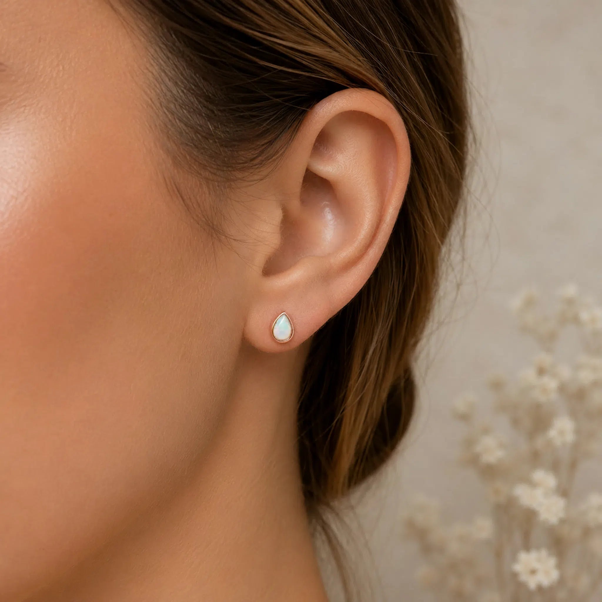 Close-up of an ear wearing a teardrop-shaped earring with a blurred background
