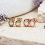 Pair of gold teardrop earrings with opal stones on a natural stone surface.