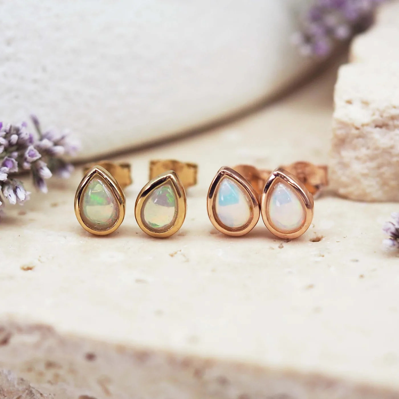 Pair of gold teardrop earrings with opal stones on a natural stone surface.
