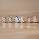 Set of six teardrop-shaped opal stones with gold, rose gold and silver prongs on a beige background