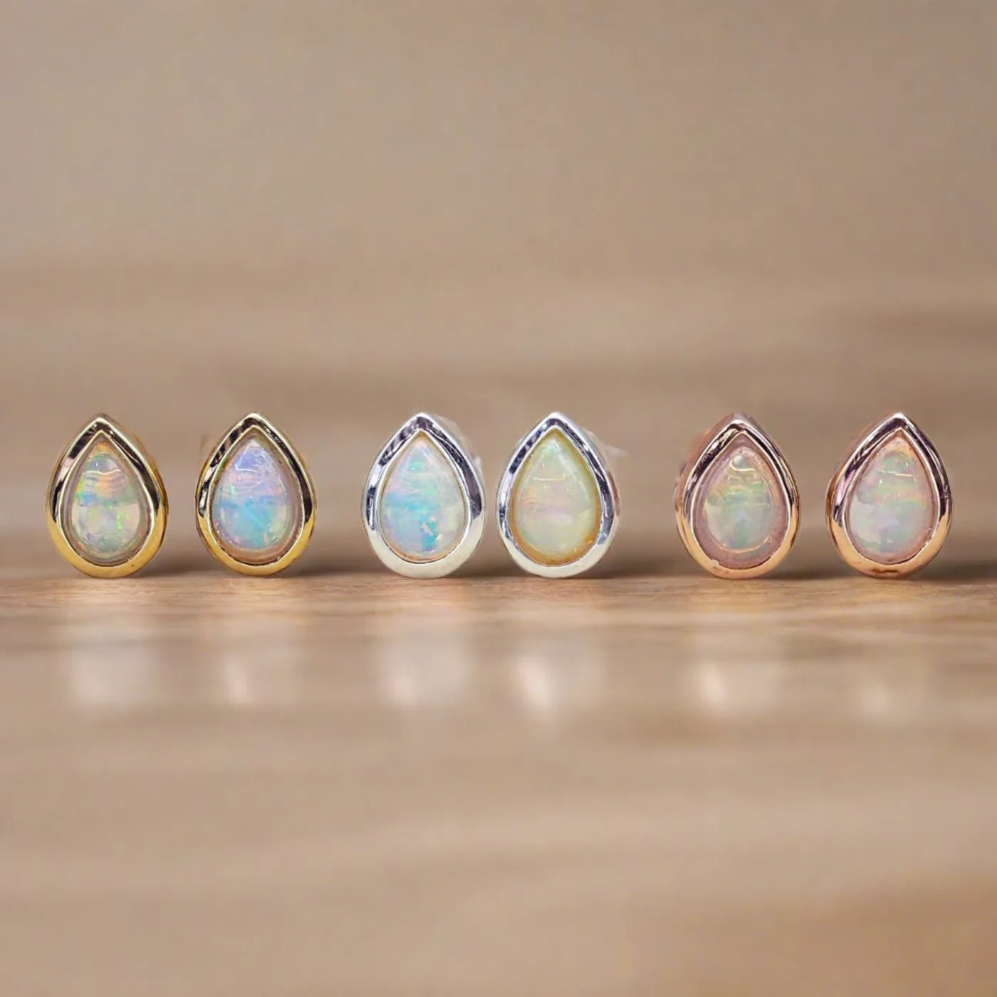 Set of six teardrop-shaped opal stones with gold, rose gold and silver prongs on a beige background