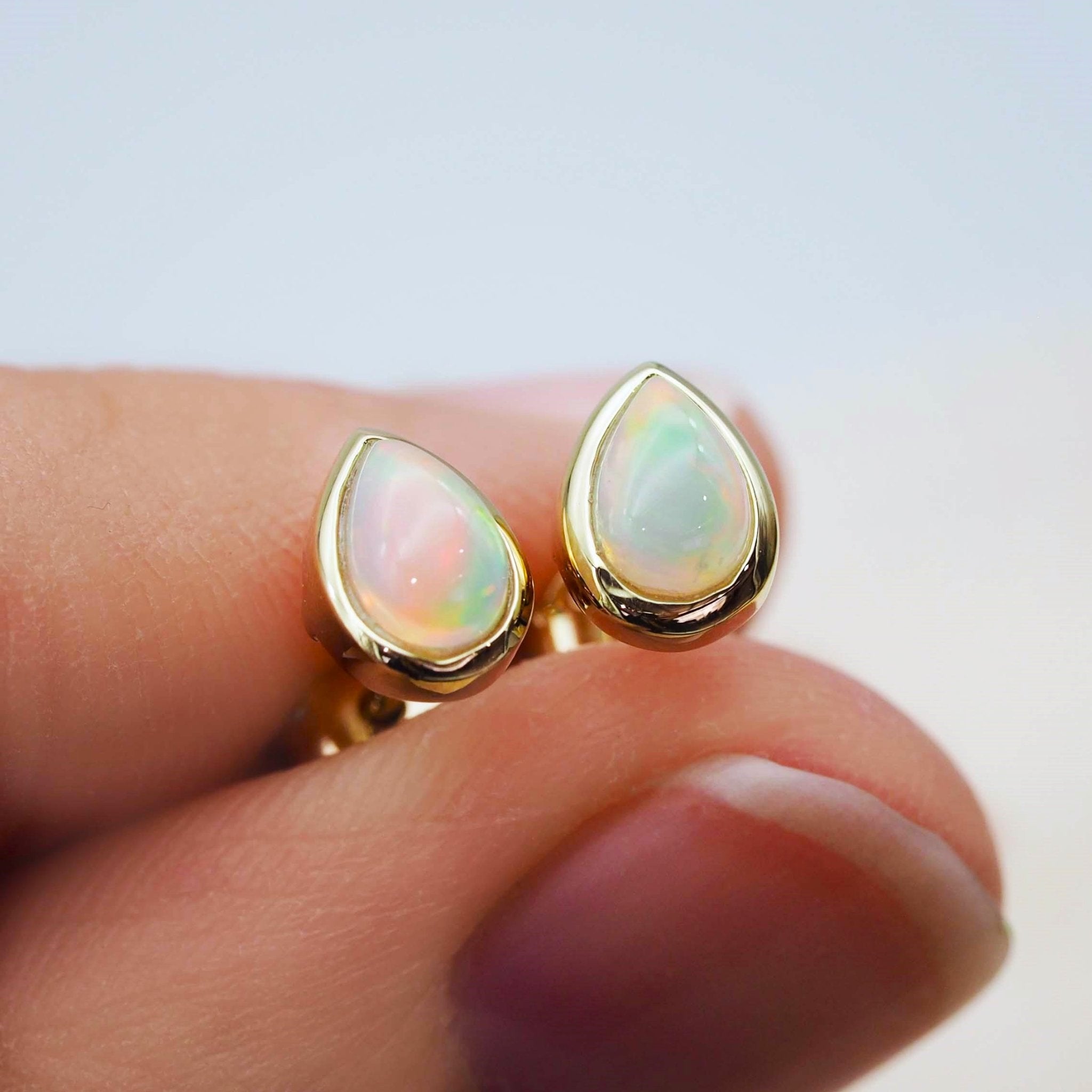 Gold october birthstone opal stud earrings being held 