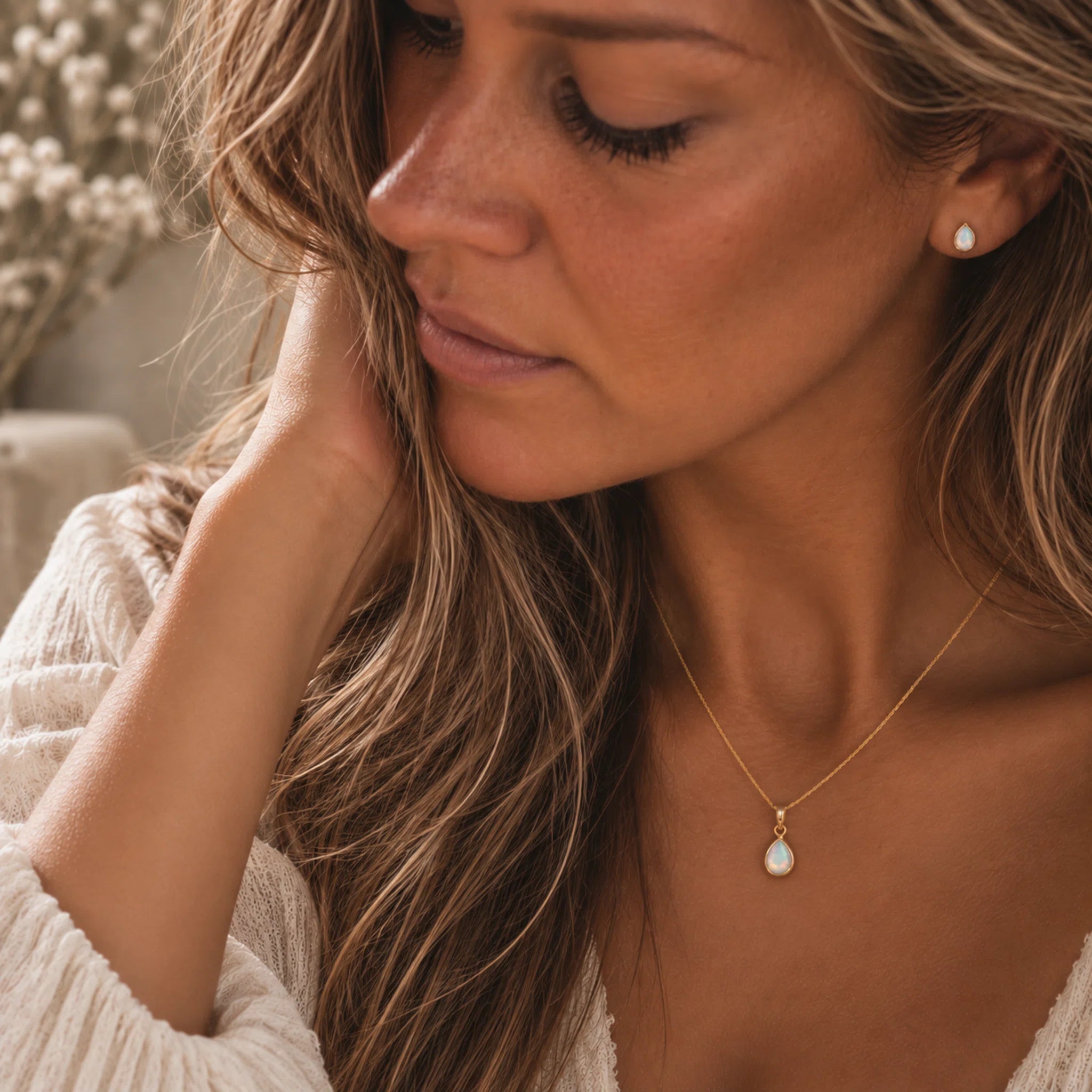 A close-up lifestyle shot of a woman wearing a october birthstone jewellery set featuring a delicate gold necklace with a teardrop-shaped natural opal pendant, paired with a matching opal stud earring.