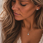 A close-up lifestyle shot of a woman wearing a delicate silver chain necklace with a teardrop-shaped natural opal stone pendant, matching a small teardrop stud opal earring.