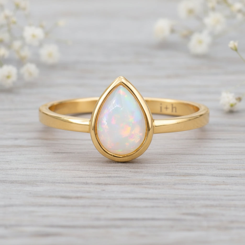 gold October birthstone ring with pear-shaped natural opal gemstone on a wooden surface - birthstone jewellery gift
