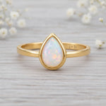 gold October birthstone ring with pear-shaped natural opal gemstone on a wooden surface - birthstone jewellery gift
