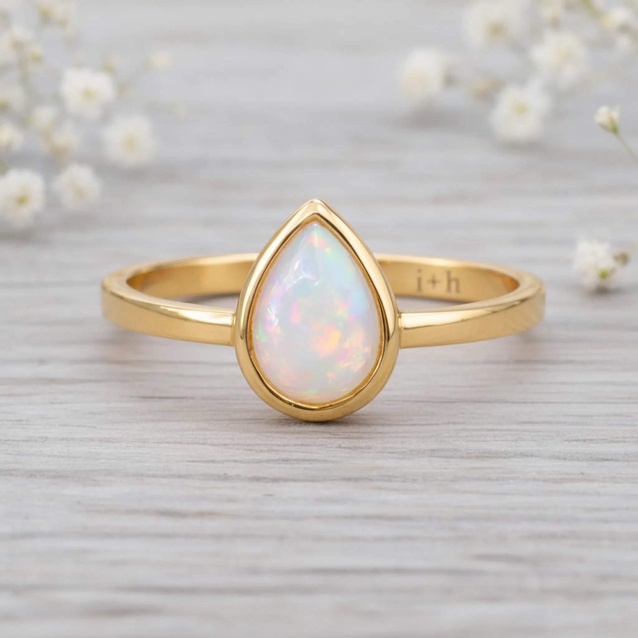 gold October birthstone ring with pear-shaped natural opal gemstone on a wooden surface - birthstone jewellery gift
