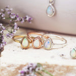 Three October birthstone rings in gold, rose gold, and silver on a textured surface with flowers.