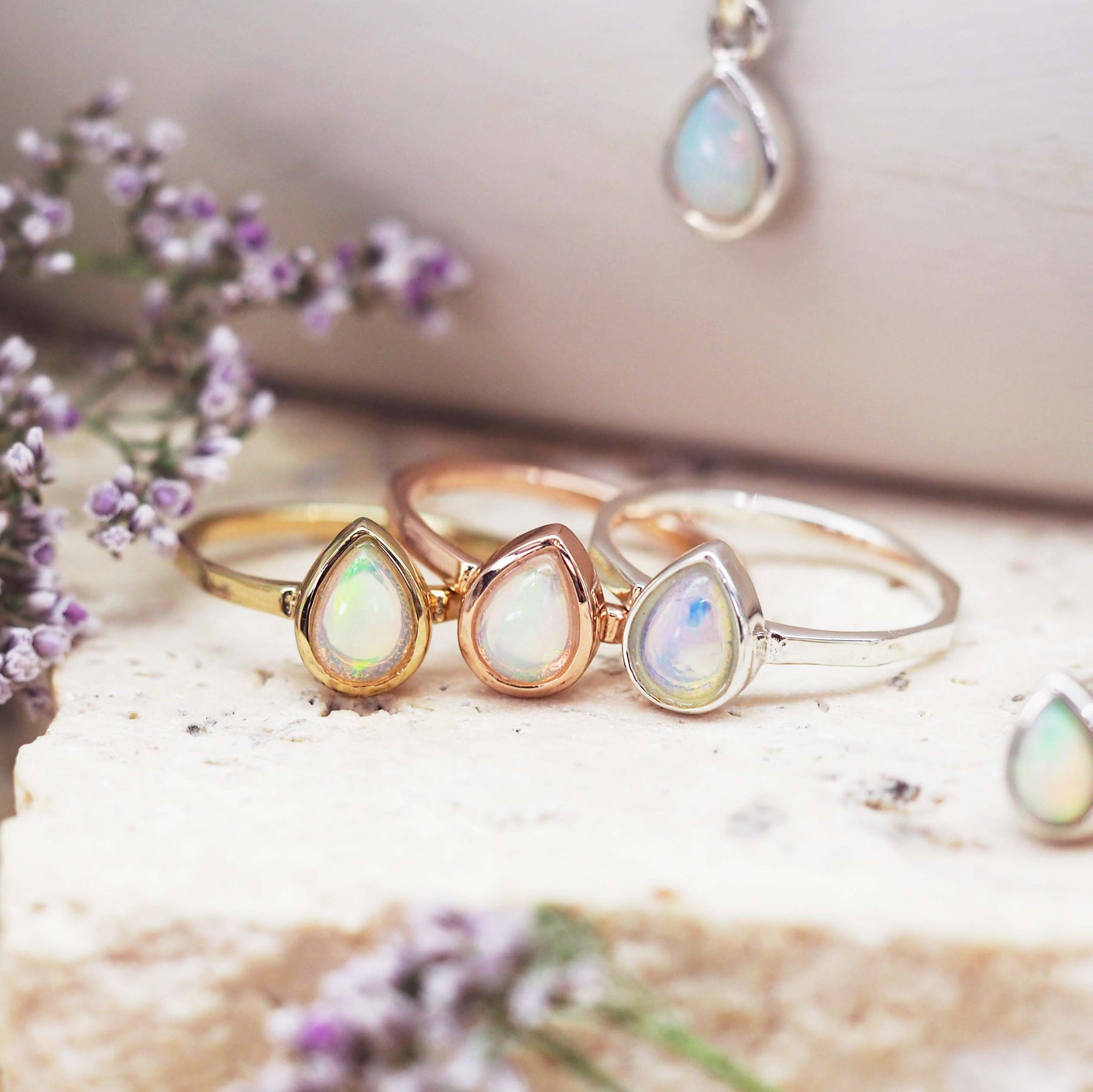 Three October birthstone rings in gold, rose gold, and silver on a textured surface with flowers.