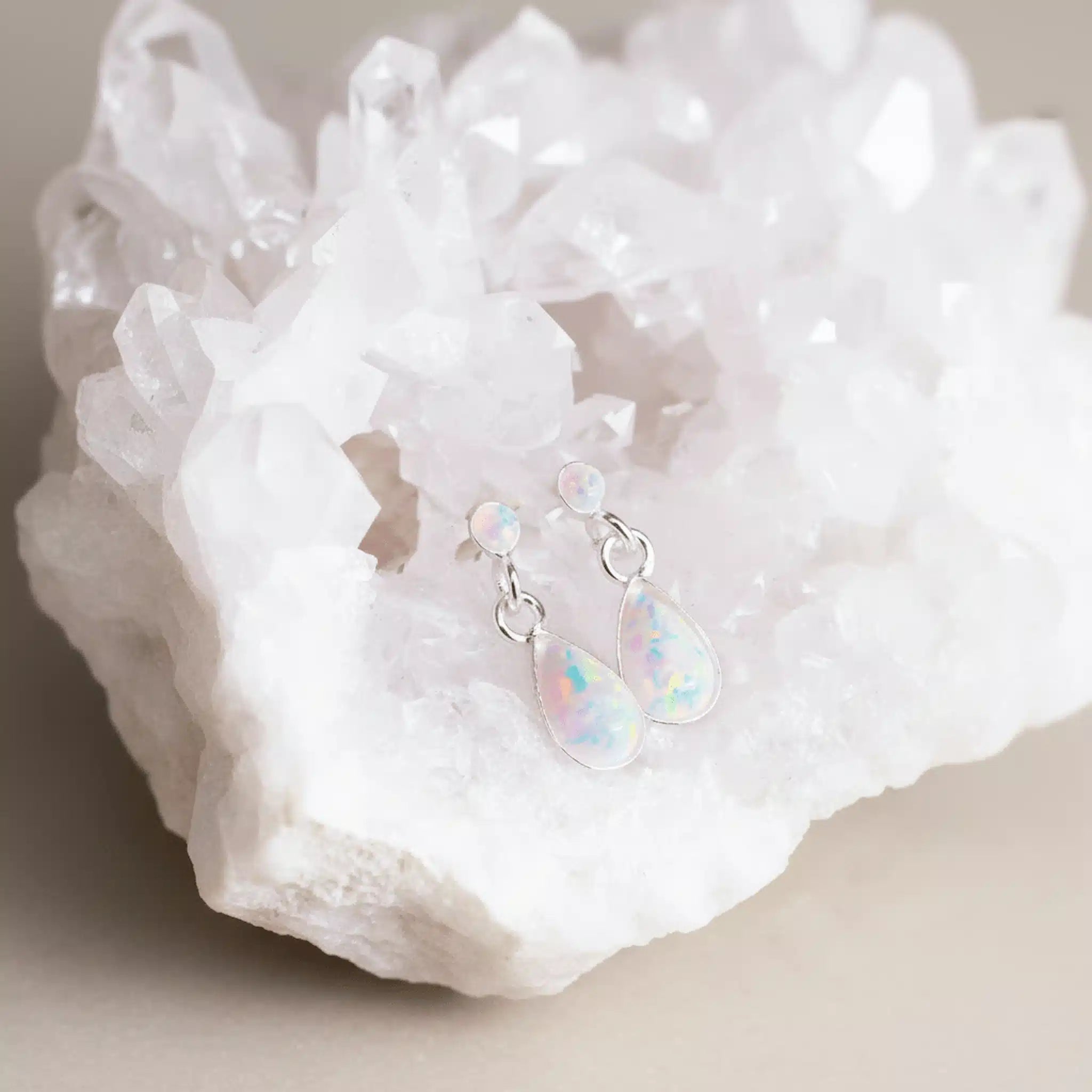 Opal teardrop earrings on a white crystal background