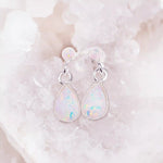 Teardrop-shaped opal earrings on a white stone background