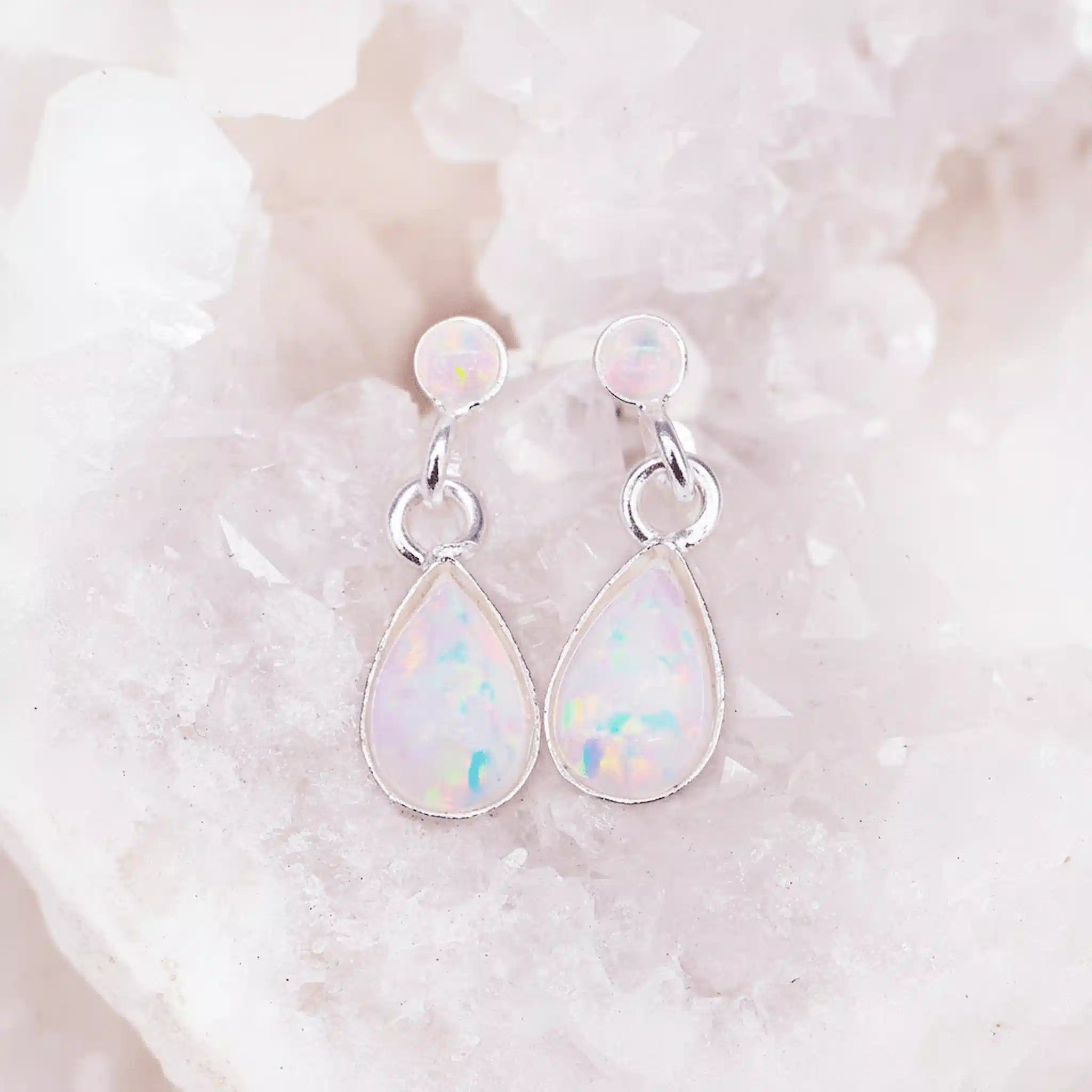 Teardrop-shaped opal earrings on a white stone background