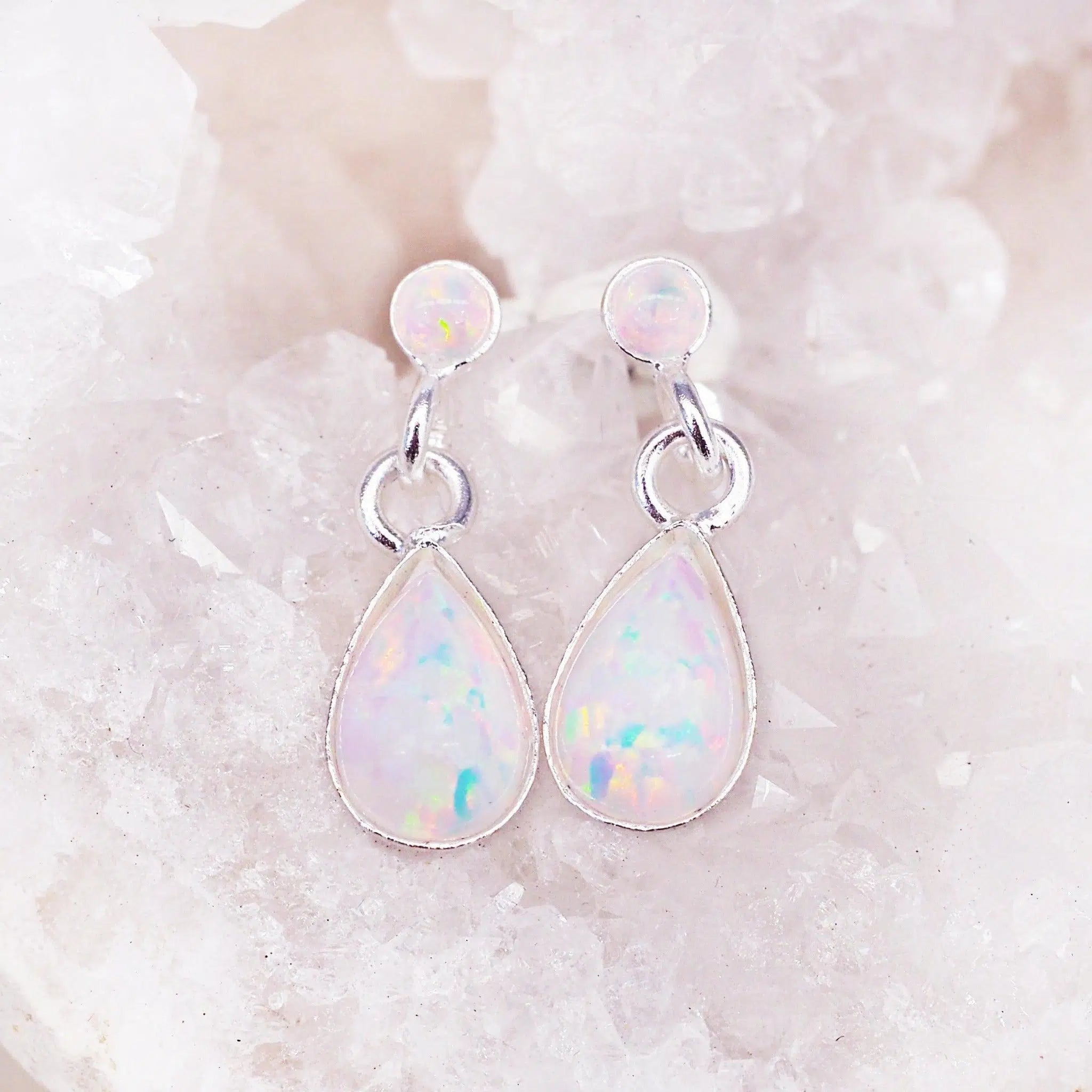 A pair of white opal earrings in sterling silver studs with teardrop white opal drop settings, displayed on crystal cluster.