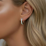 Close-up of a woman's ear wearing a silver hoop earring with small opal stones.