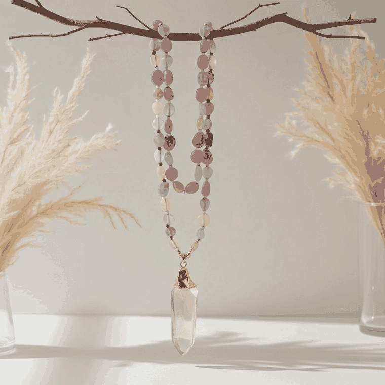 Necklace with pink and blue beads and a pink crystal pendant on a branch with dried plants.