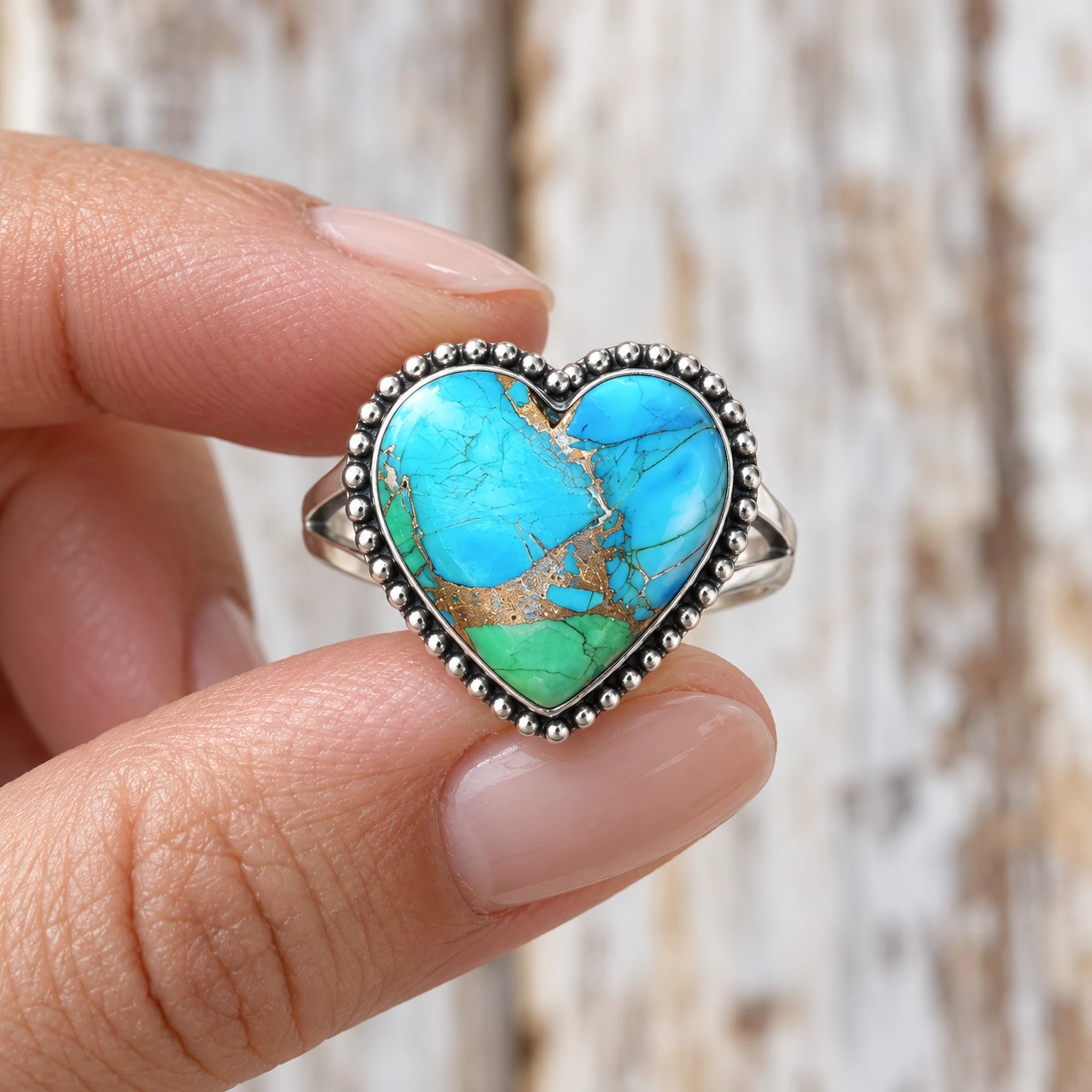 Peacock Dahlia turquoise heart ring, alternate blue and green stone with gold-coloured matrix, held between fingers
