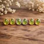 Set of green teardrop-shaped gemstone rings on a wooden surface with dried flowers in the background.