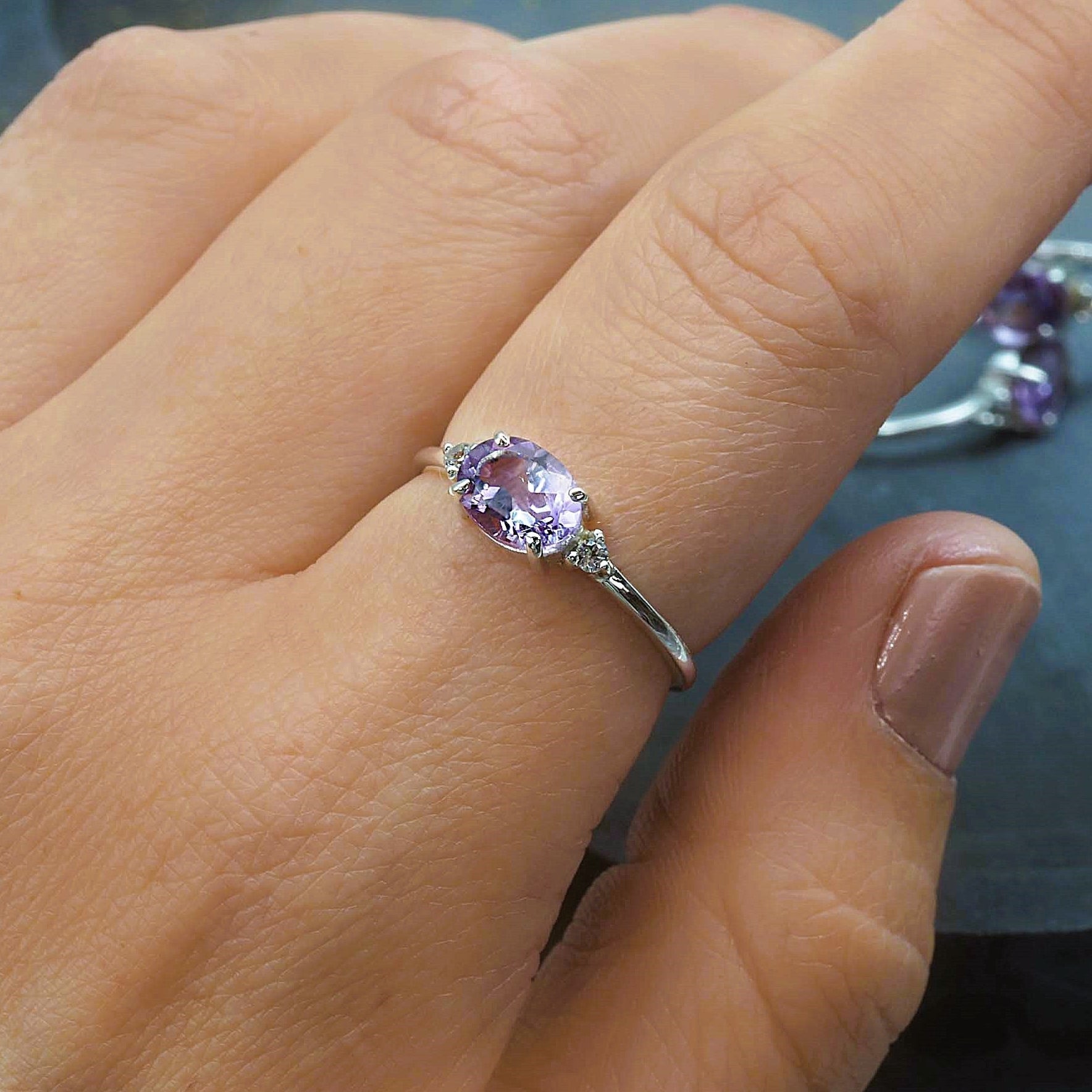 Close-up of a hand wearing a ring with a purple pink amethyst gemstone on a blurred background
