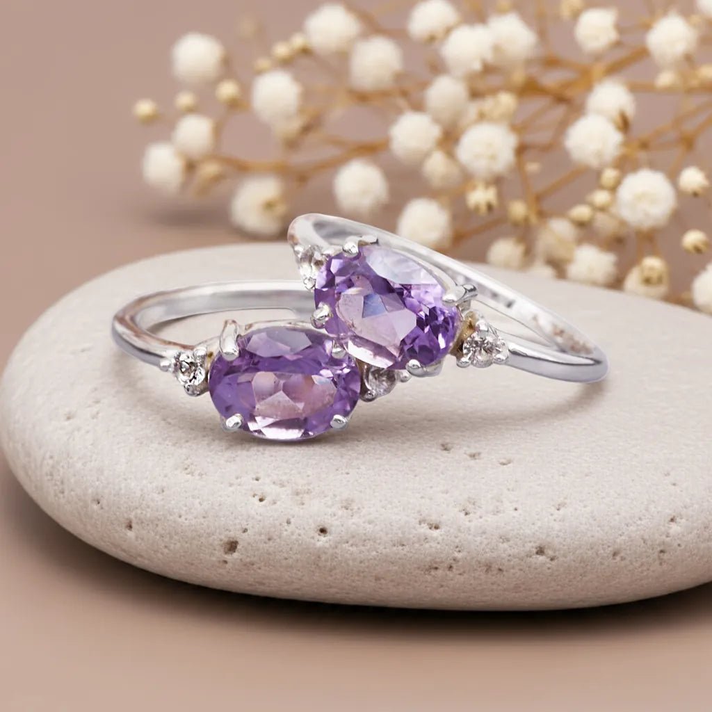Silver rings with purple pink amethyst gemstones on a stone surface with decorative flowers in the background