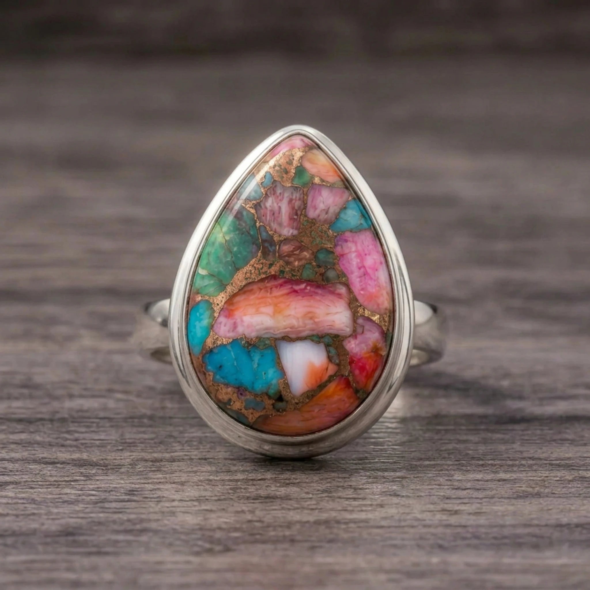 Pink copper turquoise ring front view, pink, turquoise and green stone in a sterling silver bezel on dark wood