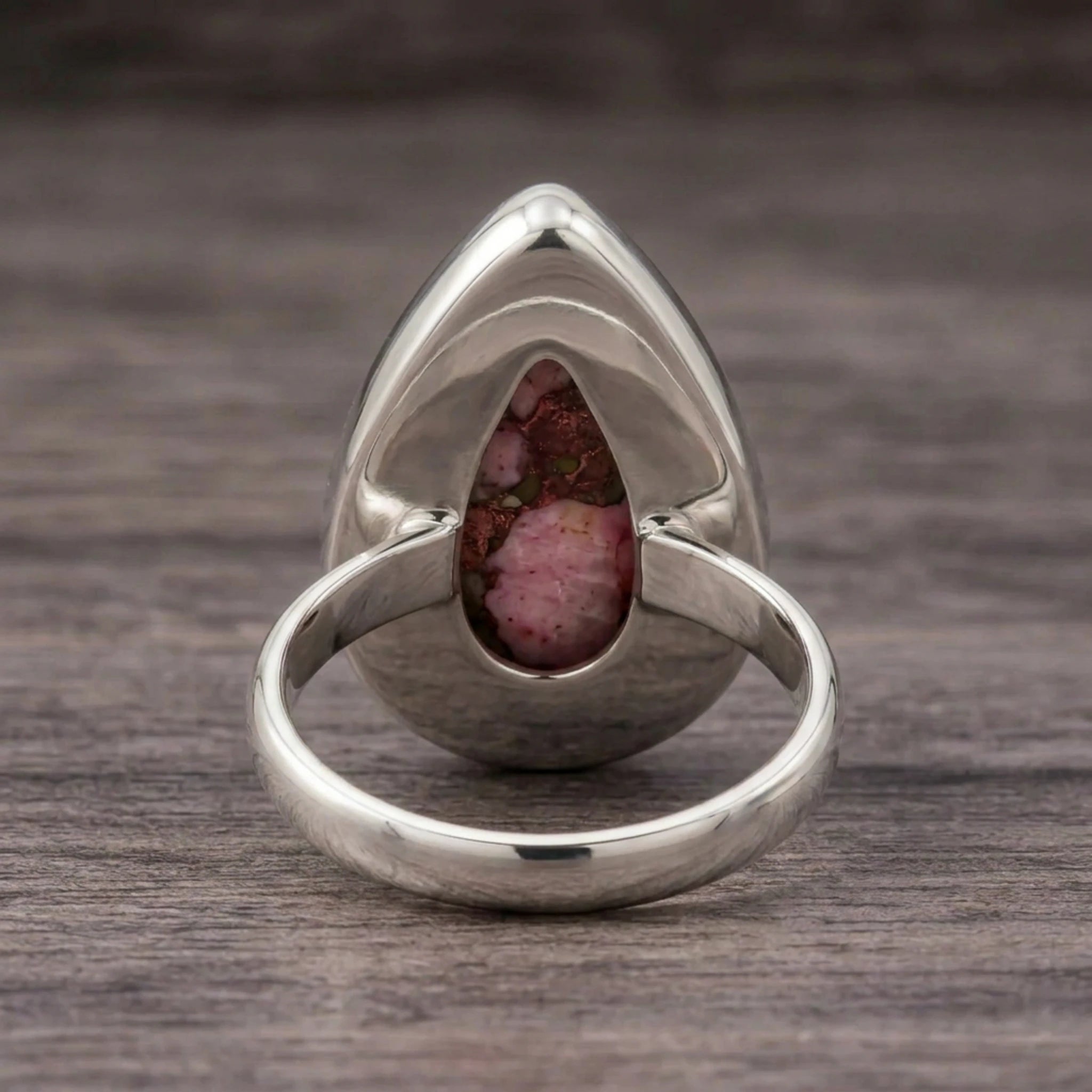 Back of the pink copper turquoise ring showing the open-back sterling silver bezel and band on dark wood