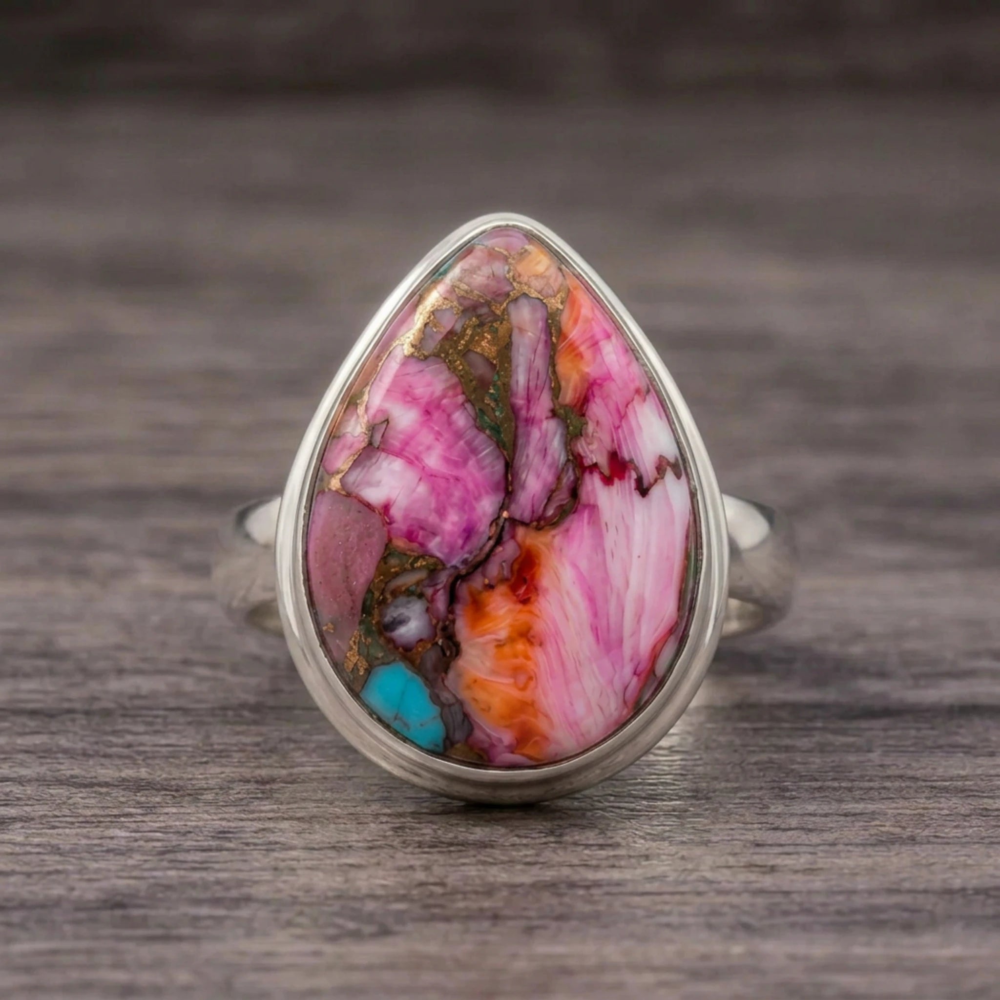 Pink copper turquoise ring front view with a mostly pink teardrop stone and copper veining on dark wood
