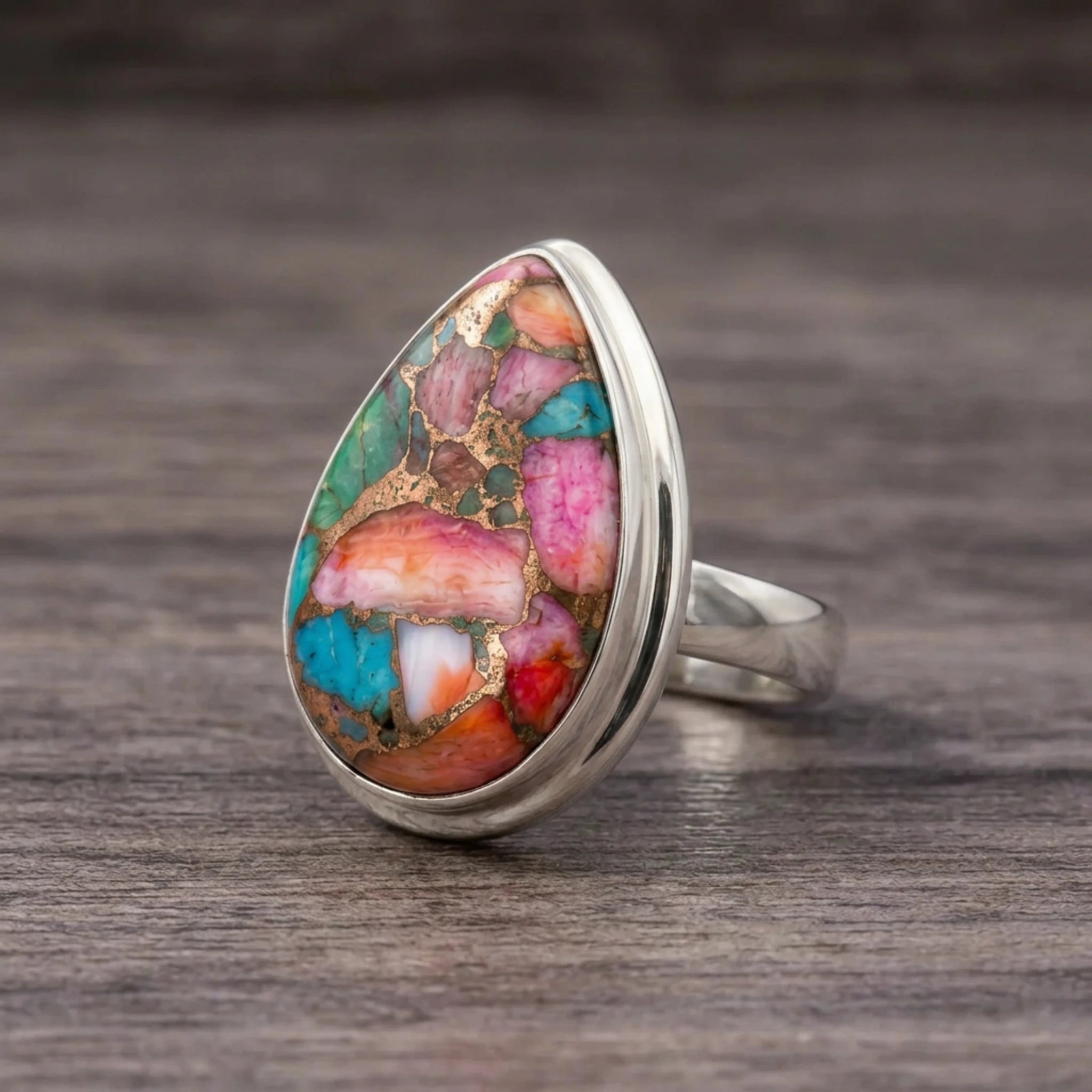 Pink copper turquoise ring side view, teardrop stone bezel set in sterling silver, lying on dark wood
