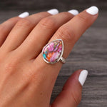 Pink copper turquoise ring worn on the index finger, pink and turquoise teardrop stone, dark wood background
