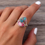 Pink copper turquoise ring worn on a hand with white nails, teardrop stone in sterling silver on dark wood