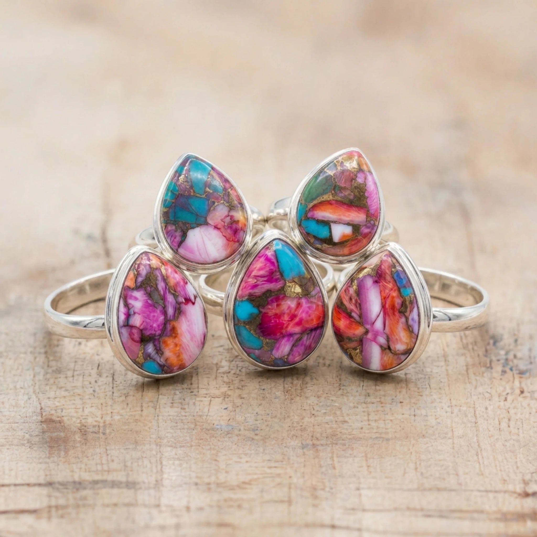 Five pink copper turquoise rings with teardrop stones in sterling silver, grouped together on pale wood