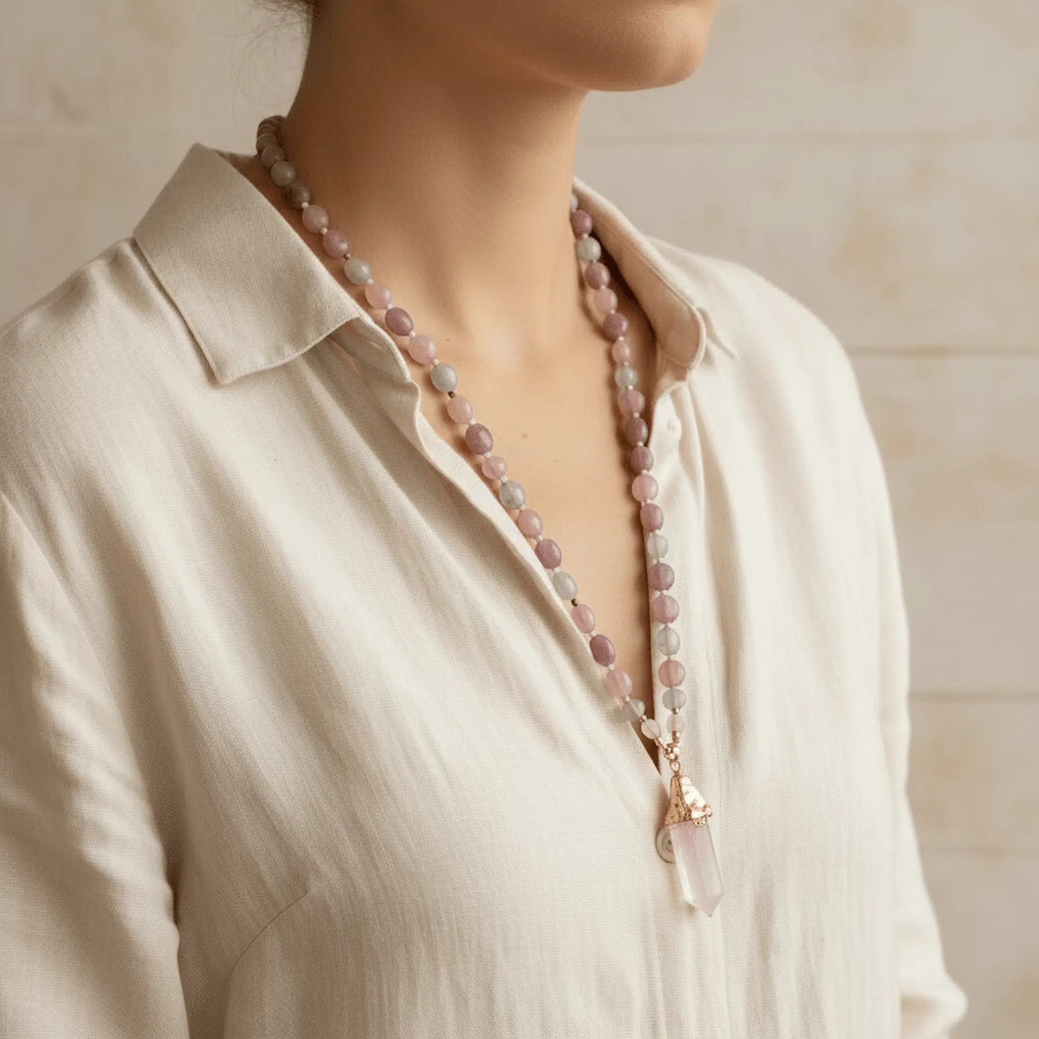 Person wearing a necklace with pink beads against a neutral background