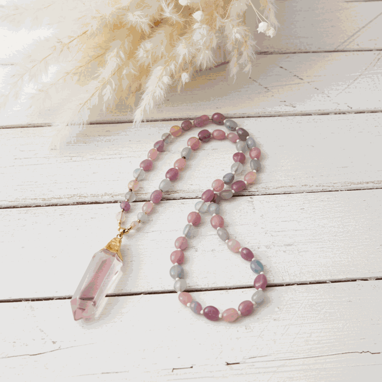 Beaded necklace with a pink crystal pendant on a light wooden surface