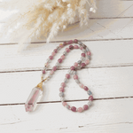 Beaded necklace with a pink crystal pendant on a light wooden surface