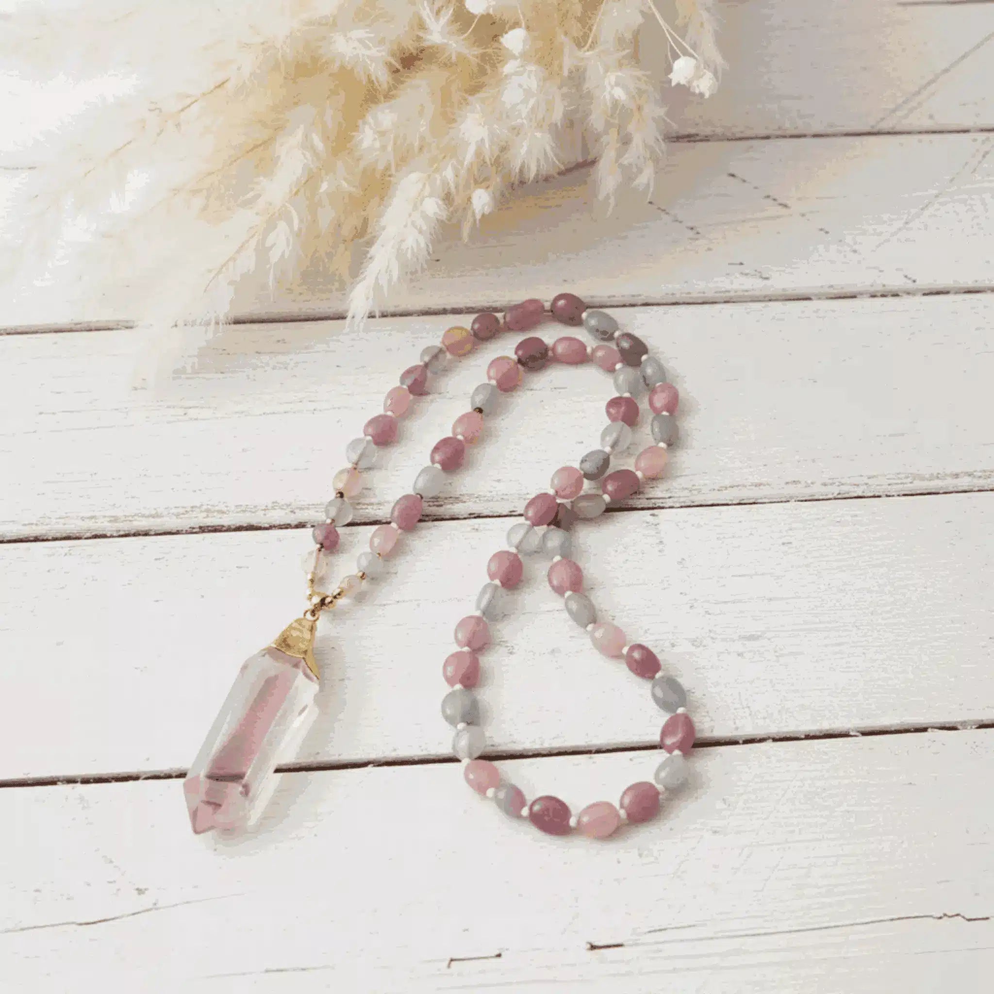Necklace with multicolored beads and a clear crystal pendant on a light wooden surface.
