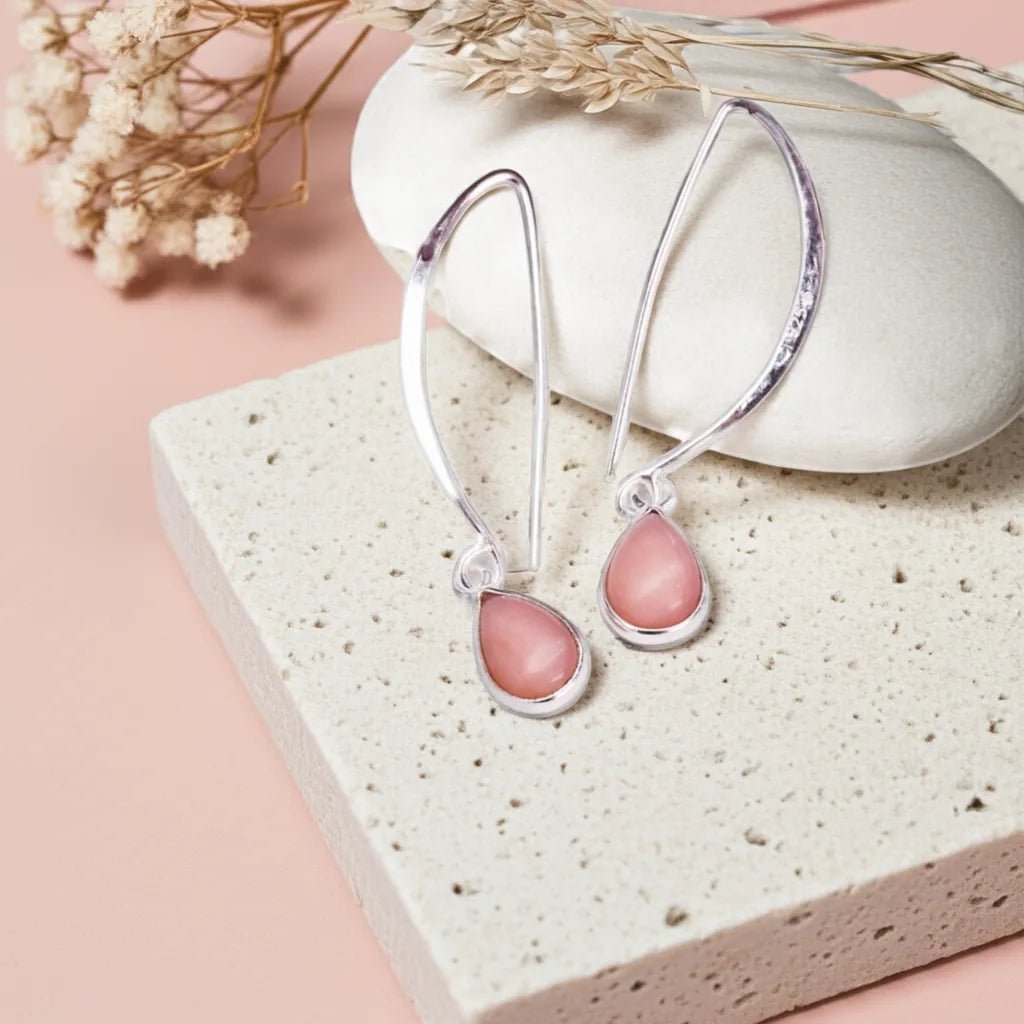 Silver earrings with pink stones on a textured stone surface with dried flowers.