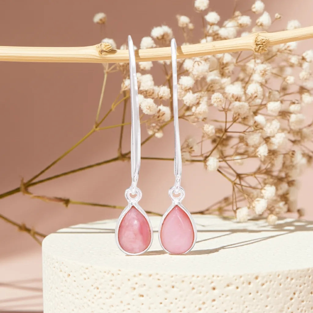Pink teardrop earrings on a decorative stand with dried flowers in the background