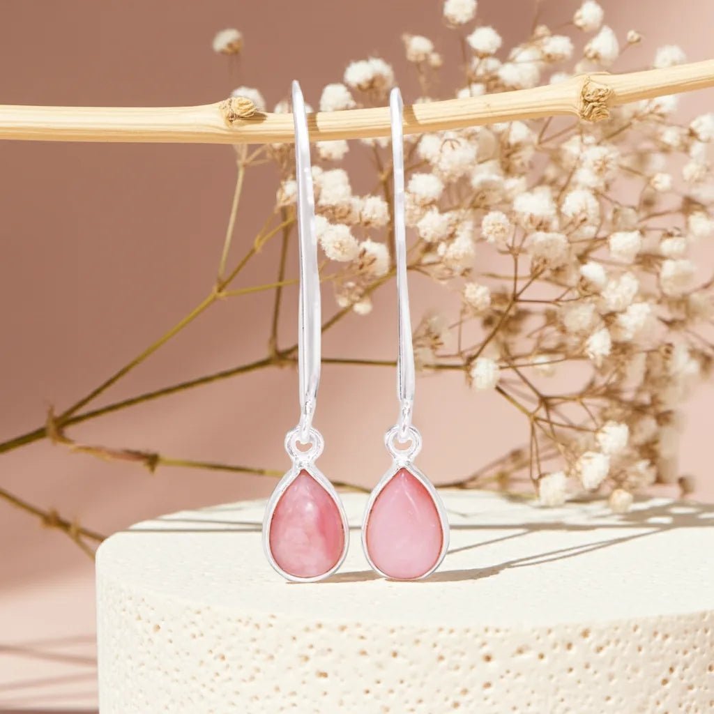 Pink teardrop earrings on a decorative stand with dried flowers in the background