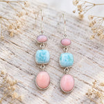 Pink opal and larimar French hook earrings on whitewashed wood with pink flowers and green leaves