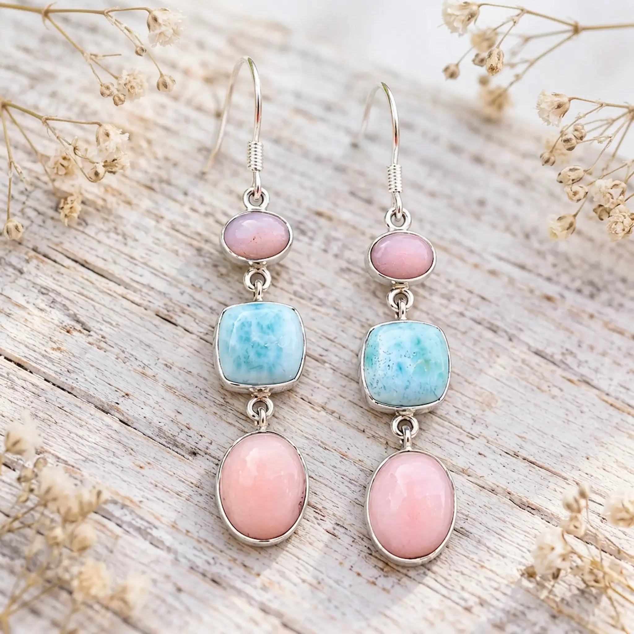 Pink opal and larimar French hook earrings on whitewashed wood with pink flowers and green leaves