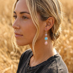 young woman wearing sterling silver french hook earrings with natural pink opal and larmiar gemstones in a field