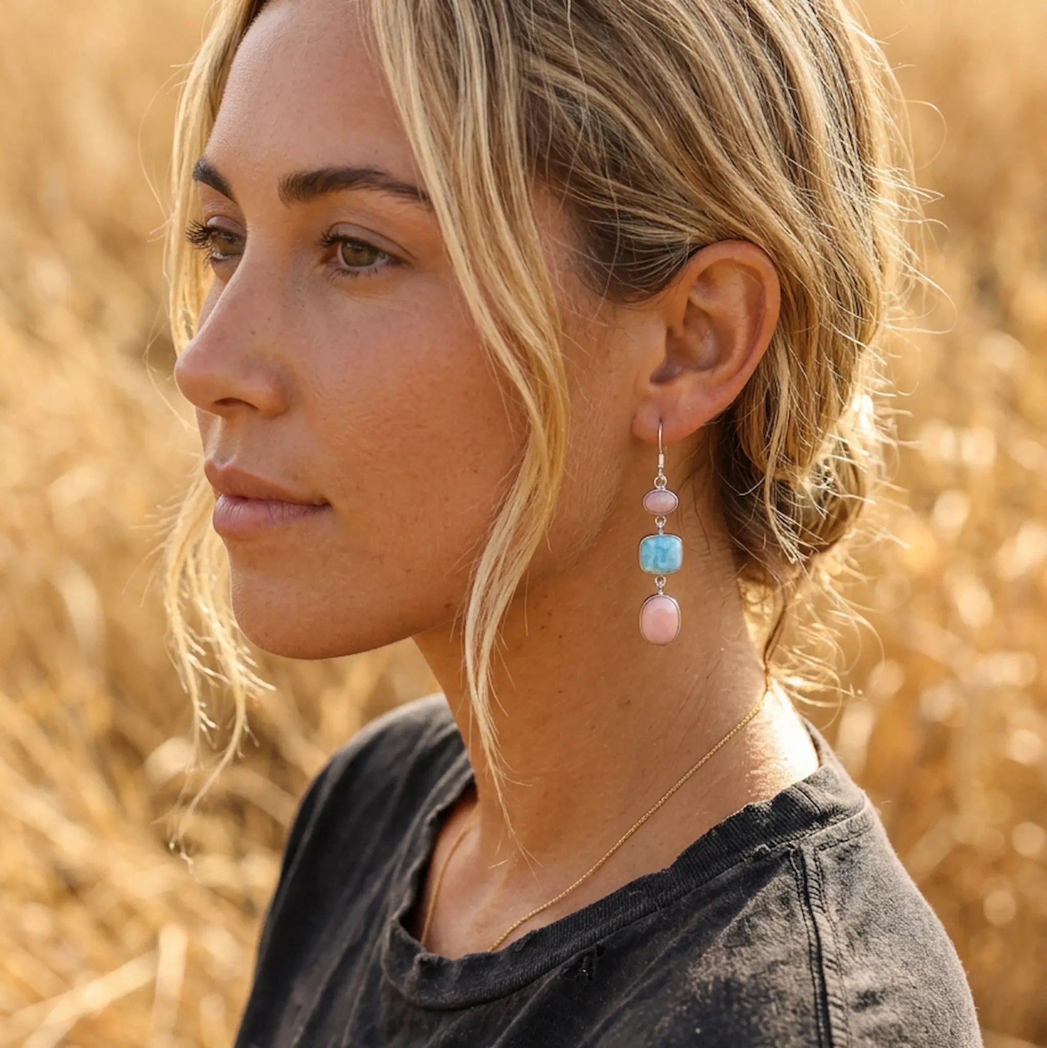 young woman wearing sterling silver french hook earrings with natural pink opal and larmiar gemstones in a field