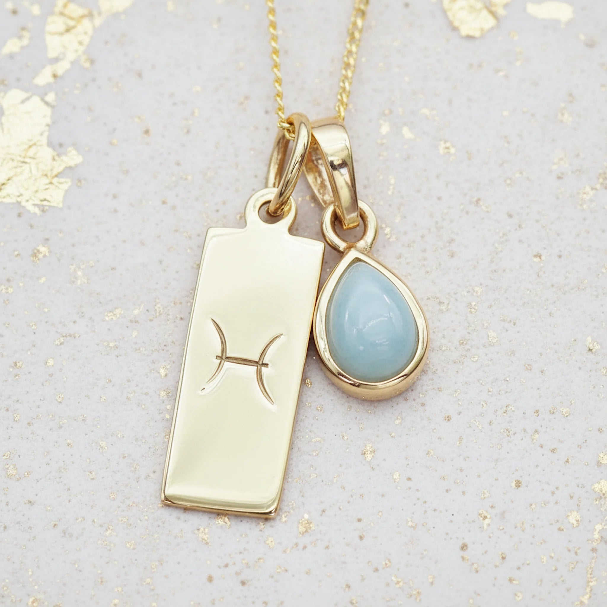 Gold necklace with a March Birthstone aquamarine pendant and a Pisces Zodiac Star Sign symbol on a textured background