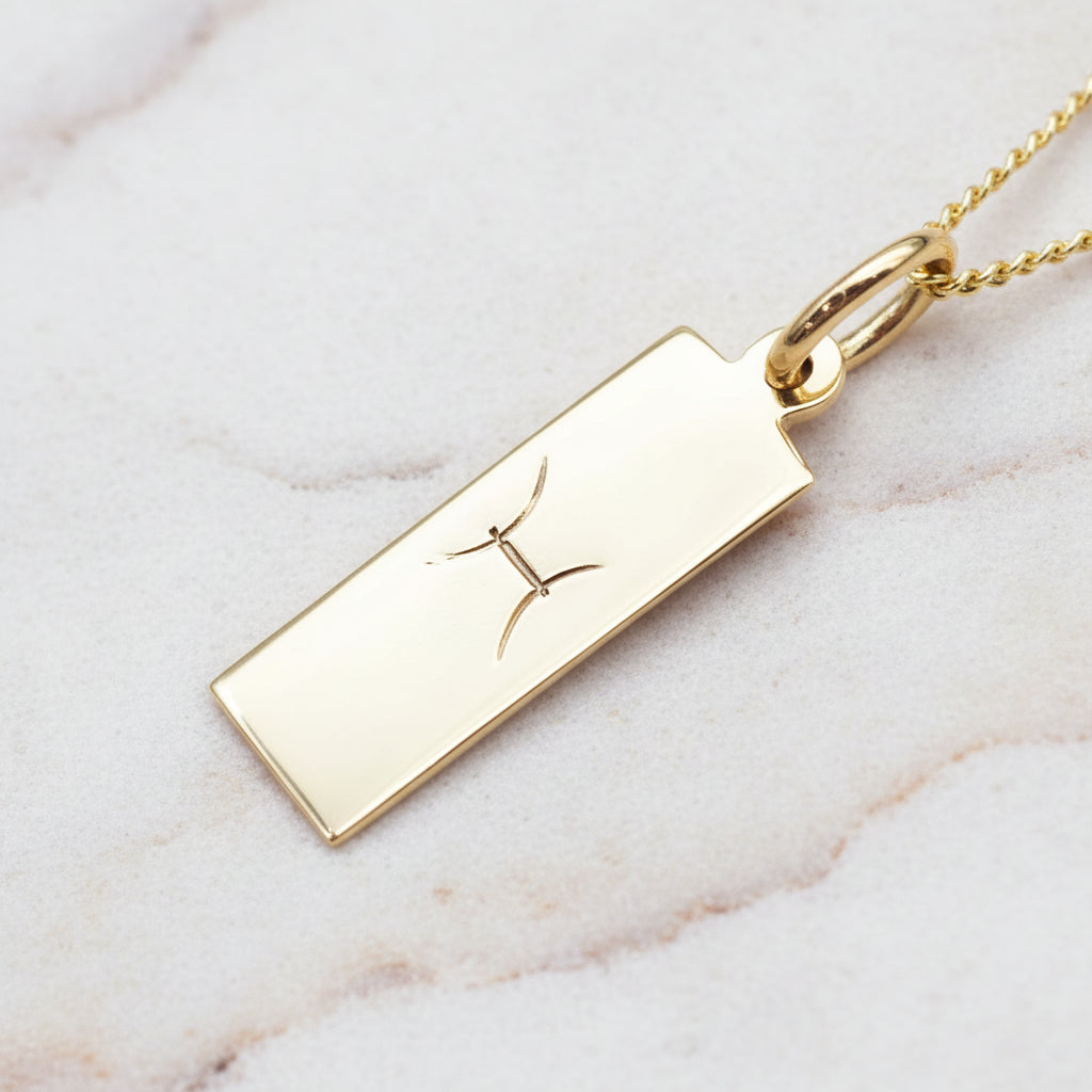 pisces zodiac necklace in gold plated sterling silver laying on  a white stone surface 