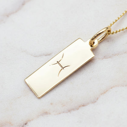 pisces zodiac necklace in gold plated sterling silver laying on  a white stone surface 