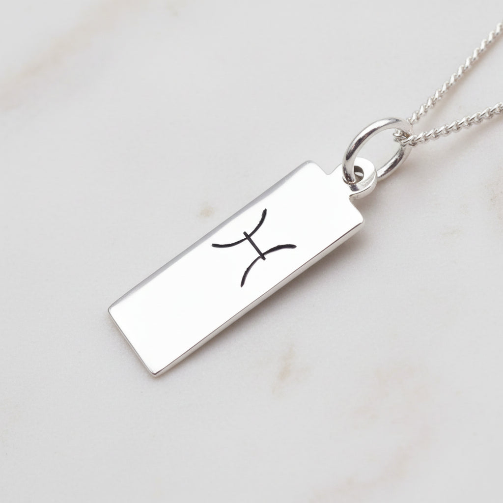 pisces zodiac necklace in sterling silver laying on a white stone surface