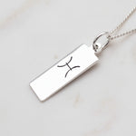 pisces zodiac necklace in sterling silver laying on a white stone surface