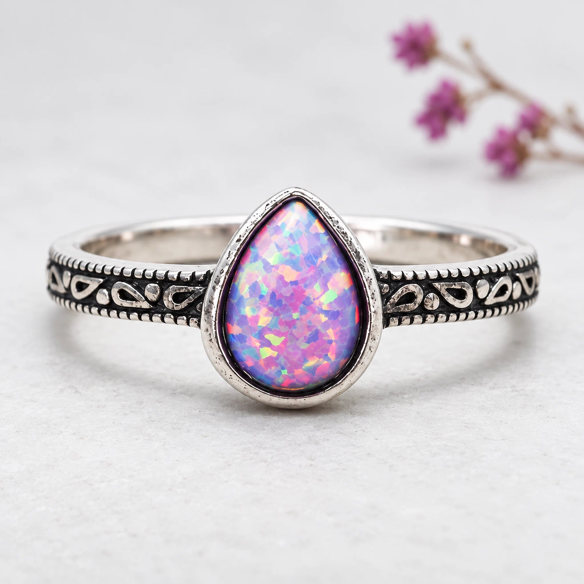 sterling Silver ring with a purple opal stone on a textured surface with pink flowers in the background